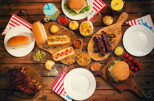 Food served at a picnic table for July 4th.On the table are traditionally grilled dishes American hamburgers,hot dogs,ribs,french fries and condiments.
