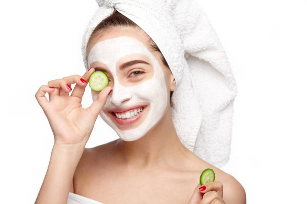 Woman moisturizing eye with cucumber Young woman with cosmetics on face applying cucumber to her eye. women facial mask mud cucumber stock pictures, royalty-free photos & images