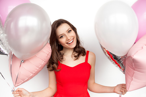 Horizontal studio shot of smiling woman holding two bunches of balloons.