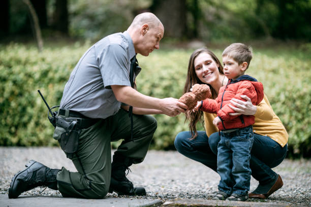 Police Officer Giving Child Stuffed Animal An on duty law enforcement officer talks to a young toddler boy and his mother, giving the child a stuffed a bear. teddy bear photos stock pictures, royalty-free photos & images