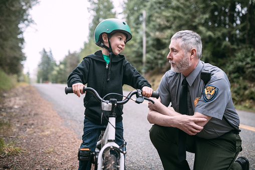 An on duty law enforcement officer talks to a young boy riding his bicycle, discussing the importance of road safety and wearing a helmet.