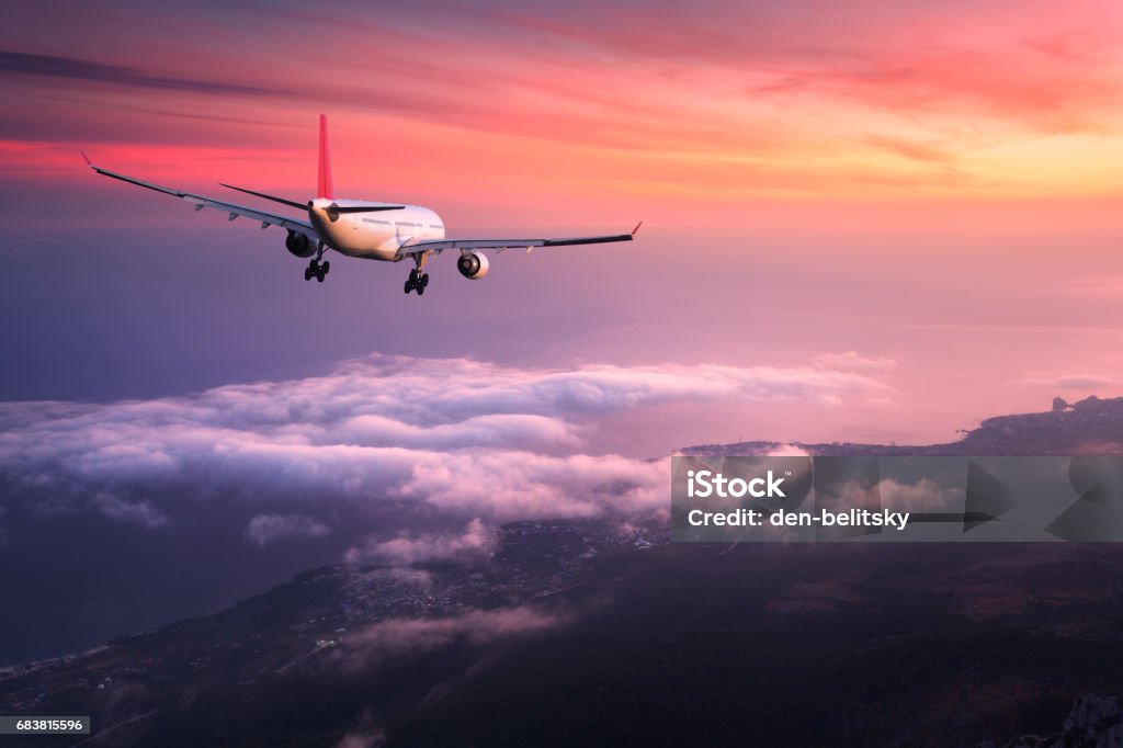 Avión. Paisaje con avión de pasajero blanco grande está volando en el cielo rojo sobre las nubes al atardecer colorido. Viaje. Avión de pasajeros es del aterrizaje al atardecer. Viaje de negocios. Avión comercial - Foto de stock de Avión libre de derechos