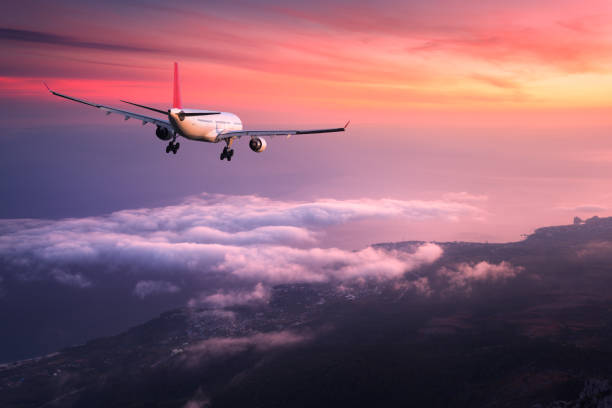 avion. paysage avec avion de passager blanc grand vole dans le ciel rouge au-dessus des nuages au coucher du soleil coloré. voyage. avion de passagers est atterrissage au coucher du soleil. voyage d’affaires. avion commercial - water jet photos et images de collection