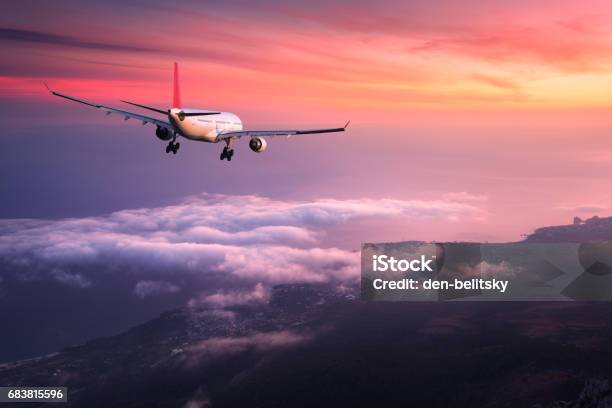 Airplane Landscape With Big White Passenger Airplane Is Flying In The Red Sky Over The Clouds At Colorful Sunset Journey Passenger Airliner Is Landing At Dusk Business Trip Commercial Plane Stock Photo - Download Image Now