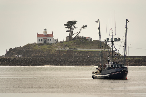 Motoring towards the pier, a fishing trawler boat named  'Spirit of America' passes in front of the Battery Point Lighthouse in Crescent City, California.
