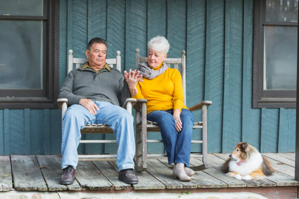 senior couple sitting on porch, holding hands, with dog - common serious couple men imagens e fotografias de stock