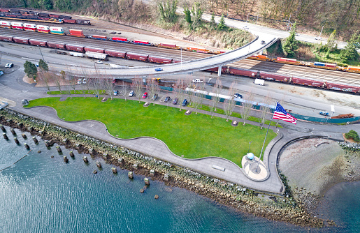 Aerial View of Thea's Grass Lawn Park With American Flag, Railroad Tracks Shipping Containers Background