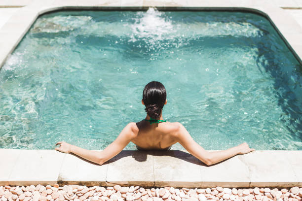 woman in green swimsuit relaxing in outdoor hot tub with clean transparent turquoise water. organic skin care in hot bath in luxury spa resort. - sensuality lifestyles cheerful comfortable imagens e fotografias de stock