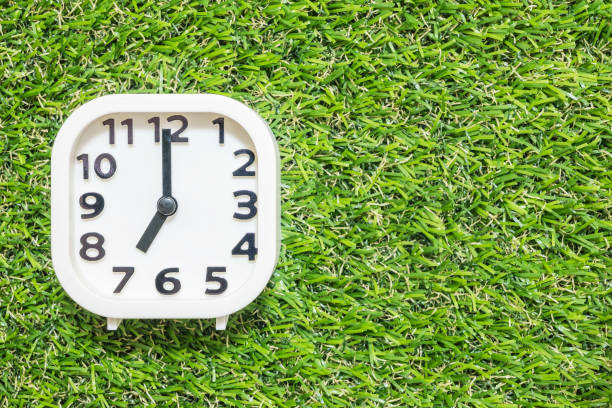 istock Closeup white clock for decorate in 7 o'clock on green artificial grass floor textured background with copy space 683882274