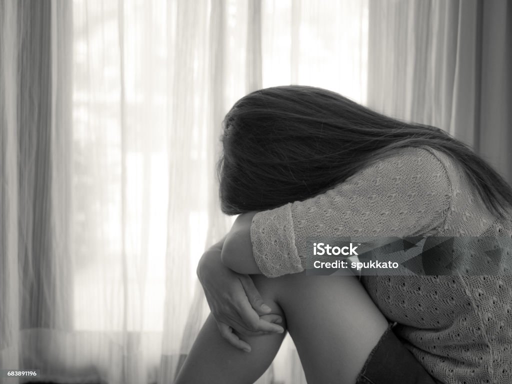 สีดําและสีขาวของผู้หญิงเศร้ากอดเข่าของเธอและร้องไห้ ผู้หญิงเศร้านั่งอยู่คนเดียวในห้องท  ภาพสต็อก - ดาวน์โหลดรูปภาพตอนนี้ - Istock