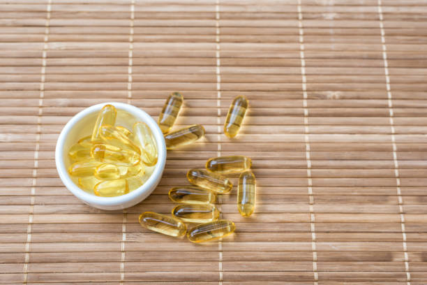 Cod liver oil omega 3 gel capsules in bowl on mat wood Cod liver oil omega 3 gel capsules in bowl on mat wood cod liver oil fish oil vitamin a pill stock pictures, royalty-free photos & images