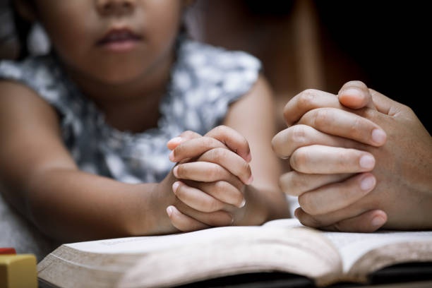 Mother and little girl hands folded in prayer on a Holy Bible together Mother and little girl hands folded in prayer on a Holy Bible together  for faith concept in vintage color tone worshipper photos stock pictures, royalty-free photos & images