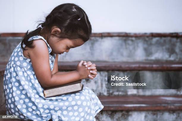 Linda Niña De Asia Cerró Los Ojos Y Dobla La Mano En La Oración En La Santa Biblia Foto de stock y más banco de imágenes de Niño