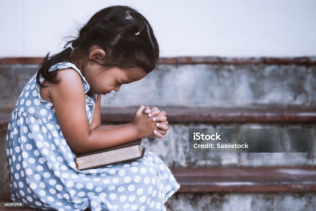 Cute asian little girl closed her eyes and  folded her hand in prayer on a Holy Bible Cute asian little girl closed her eyes and  folded her hand in prayer on a Holy Bible for faith concept in vintage color tone Praying Stock Photo
