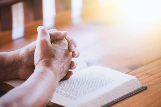 пожилая женщина руки сложены в молитве на библии - praying women senior adult spirituality стоковые фото и изображения