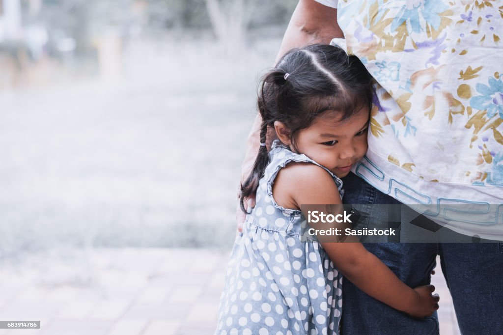 Triste niña asiática abraza la pierna de la madre - Foto de stock de Niño libre de derechos