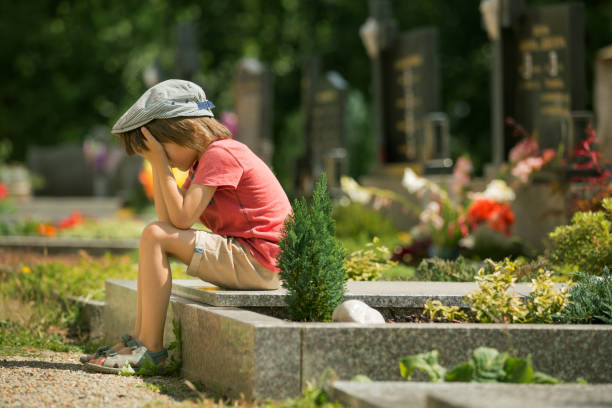 istock Sad little boy, sitting on a grave in a cemetery, feeling sad and crying 683927364