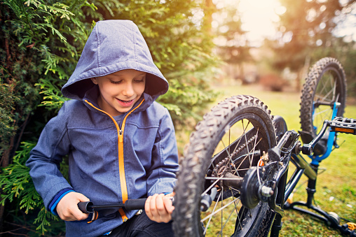 Little boy aged 7 tending to his bicycle in the garden. The boy is inflating the tires.
