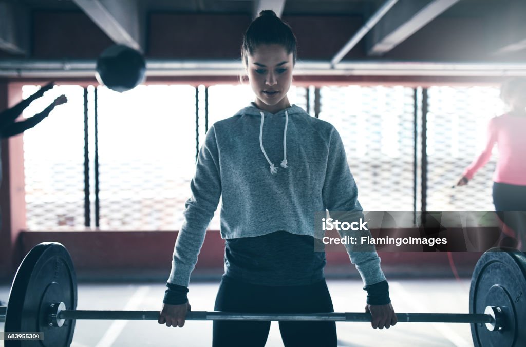 Fit healthy woman lifting a weight barbell Fit healthy woman lifting a weight barbell, exercising with group of people, looking determined and focused Weightlifting Stock Photo