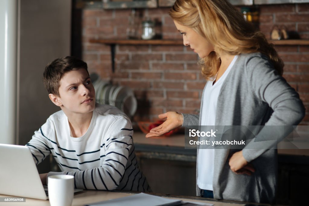 Attentive boy looking at his mother I will not punish. Pretty delighted female standing in semi position and putting left hand on the belt while talking to her son Teenager Stock Photo