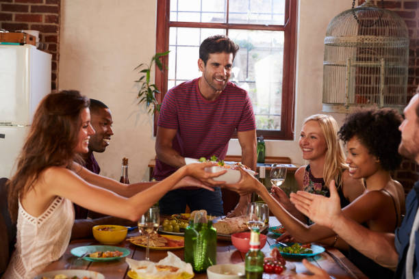 host y amigos pasan alimentos alrededor de una mesa en una cena - face to face twilight togetherness vertical fotografías e imágenes de stock