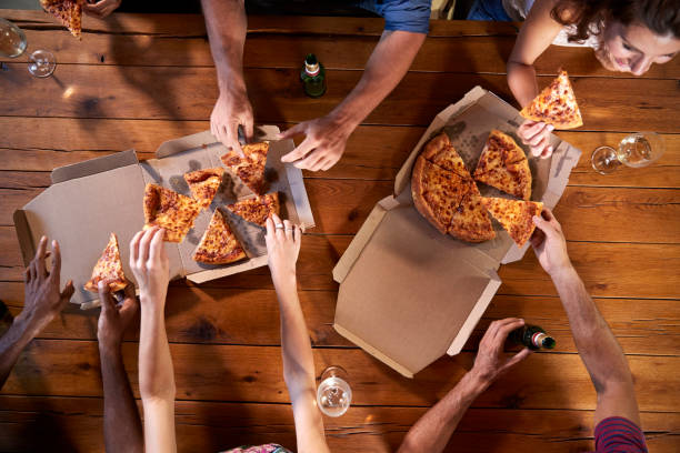 overhead schuss von freunden an einem tisch, take-away pizza teilen - speisen oder getränke zum mitnehmen stock-fotos und bilder