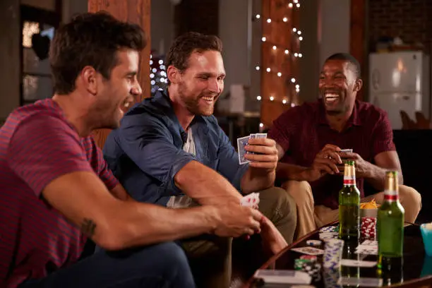 Three male friends playing cards and laughing at home