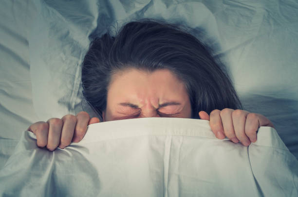 istock Woman with stressed face expression eyes closed hiding behind sheet in bed 684029374