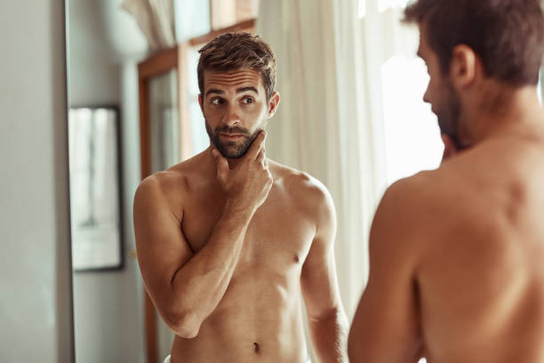 He's serious about his skincare Shot of a shirtless man checking out his skin in the bathroom mirror semi dress stock pictures, royalty-free photos & images