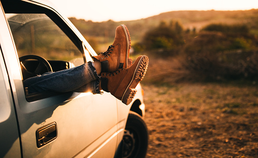 Woman's boots hanging out of an old car window on a country road trip