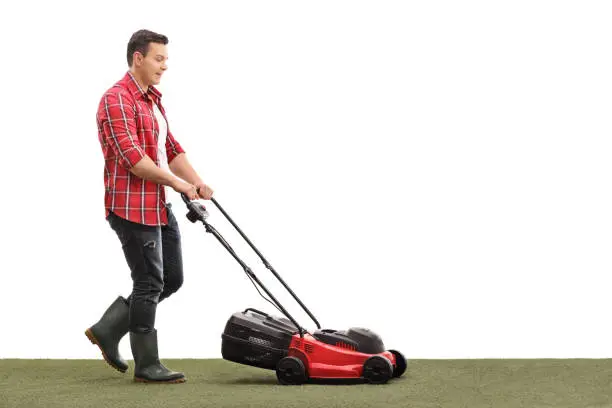 Full length profile shot of a gardener mowing a lawn with a lawnmower isolated on white background