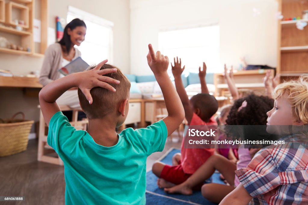 Pupilas na escola de Montessori que levanta as mãos para responder à pergunta - Foto de stock de Criança royalty-free