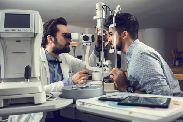 Mid adult ophthalmologist measuring an eyesight of a young man with diagnostic medical tool. Male ophthalmologist examining young man's eyesight with optical instrument. eye test equipment stock pictures, royalty-free photos & images