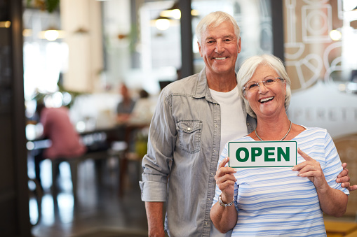 Portrait of a happy senior couple holding up an open sign in their store