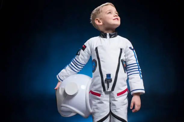 Cute little boy in space suit holding helmet and looking at distance