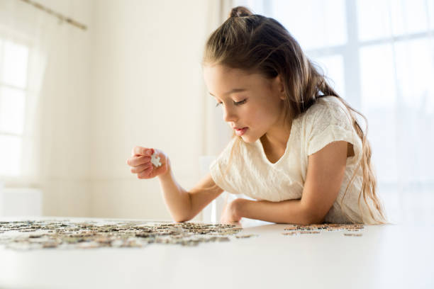 side view of concentrated little girl playing with puzzles at home stock photo