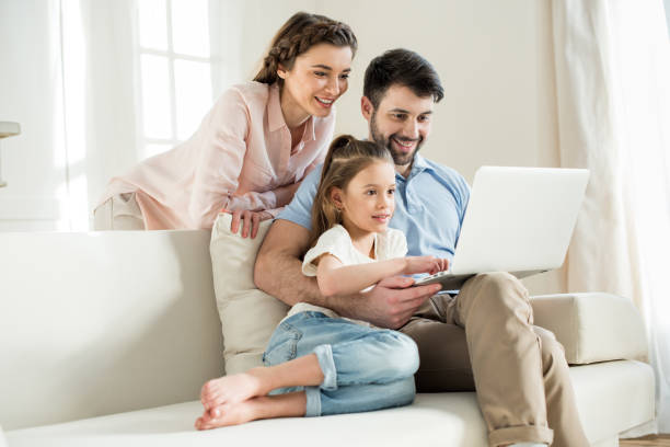 istock smiing parents and focused daughter using laptop at home 684098400