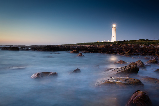A horizontal composition of the lighthouse in Cape St. Francis in the Eastern Cape province of South Africa, reflected in the blue tones of the pre-dawn ocean.