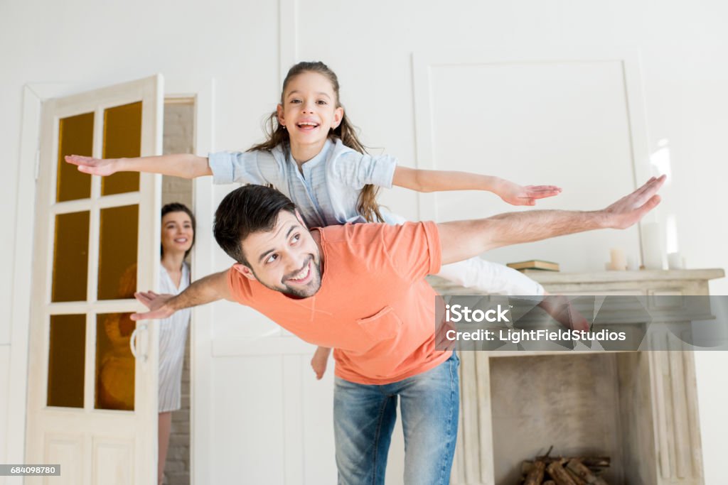 smiling mother watching how father playing with daughter Family Stock Photo