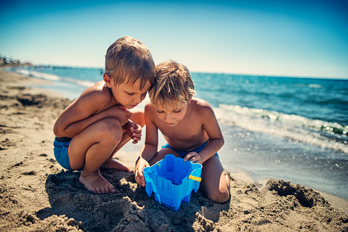Little boys playing on italian beach in Tuscany. The boys are observing a jellyfish caught in sand bucket full of water.


