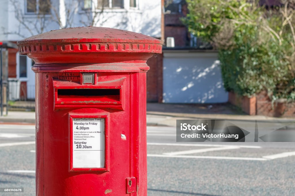Red English post box set against a de-focused street background Red English post box set against a de-focused street background in London Postal Worker Stock Photo