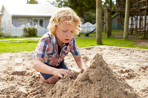 Male Pupil At Montessori School Playing In Sand Pit At Breaktime