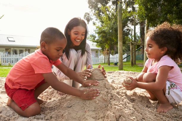 砂場で子どもたちと遊ぶモンテッソーリ学校の先生 - african ethnicity student child group of people ストックフォトと画像