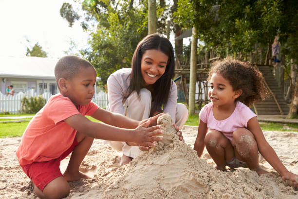 Teacher At Montessori School Playing With Children In Sand Pit Teacher At Montessori School Playing With Children In Sand Pit sandbox stock pictures, royalty-free photos & images