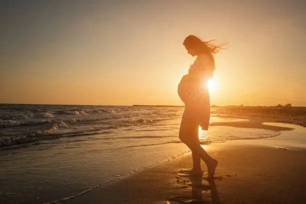 Photo of Silhouette of pregnant woman on beach in the sea sunset