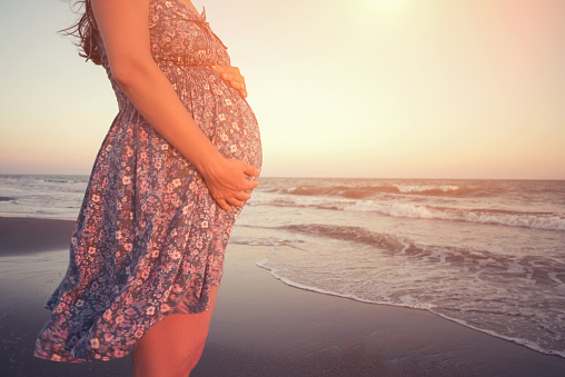 Pregnant woman holding her belly on the beach with copy space