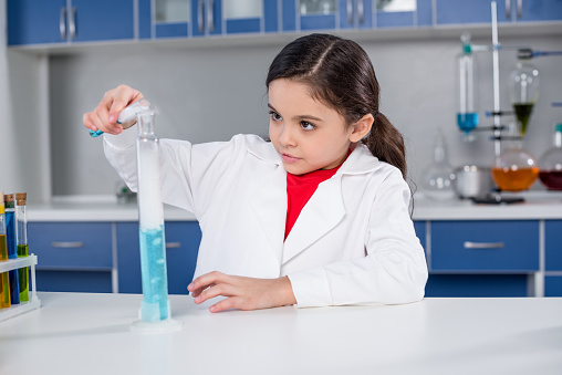 Concentrated little girl in lab coat making experiment in chemical laboratory