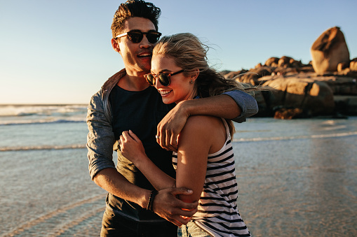 Outdoor shot of romantic young couple together on beach. Young man and woman in love on seashore.