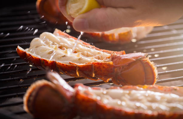 Grilled Lobster Tail on the Grill with Lemon Fresh cold water lobster tails being cooked on a outdoor grill with fresh lemon juice being squeezed on the tails. Lobster Tail stock pictures, royalty-free photos & images