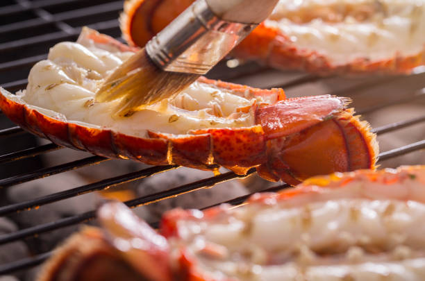 Fresh cold water lobster tails being cooked on a outdoor grill and being basted with butter and lemon